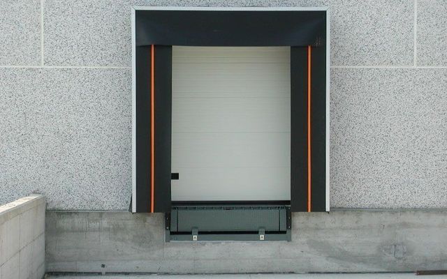 Un edificio grigio con una porta bianca e una tenda da sole nera