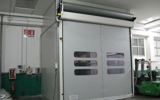 Un carrello elevatore verde è parcheggiato davanti a una grande porta in un magazzino.