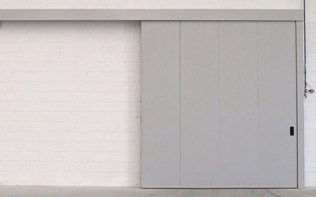 Una porta scorrevole grigia è appoggiata a un muro di mattoni bianchi.