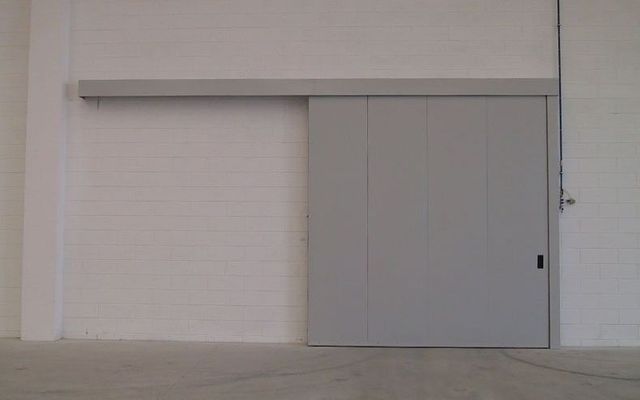 Una porta scorrevole grigia è appesa a una parete bianca in una stanza vuota.
