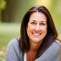 Smiling woman in a gray sweater outdoors with a blurred green background