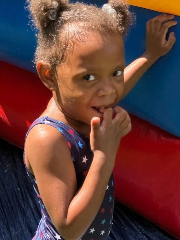 A young person with hair in two buns wears a star-patterned swimsuit while playing near a colorful inflatable structure.