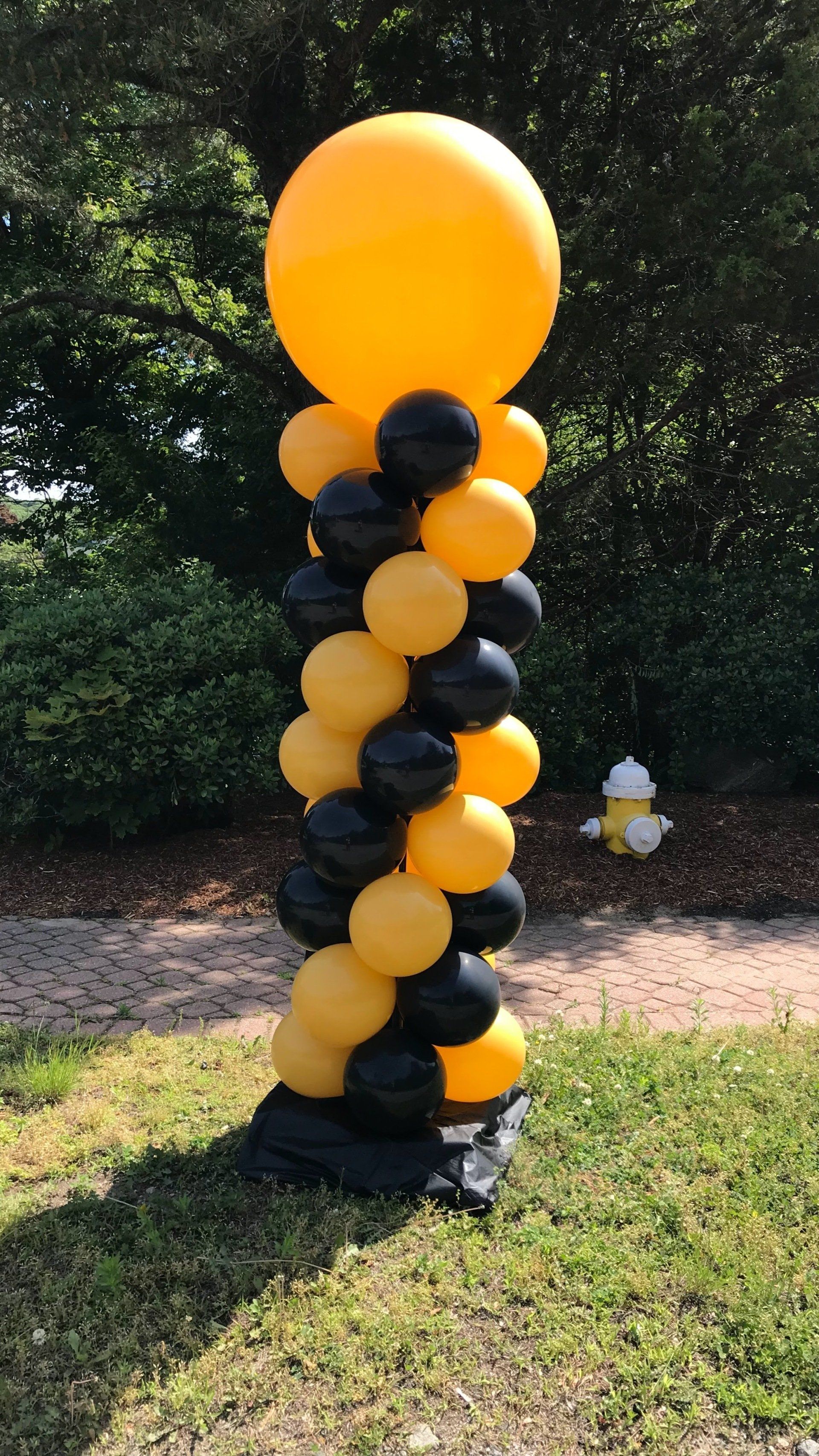 Black and gold balloon column with large yellow balloon on top, outdoors.