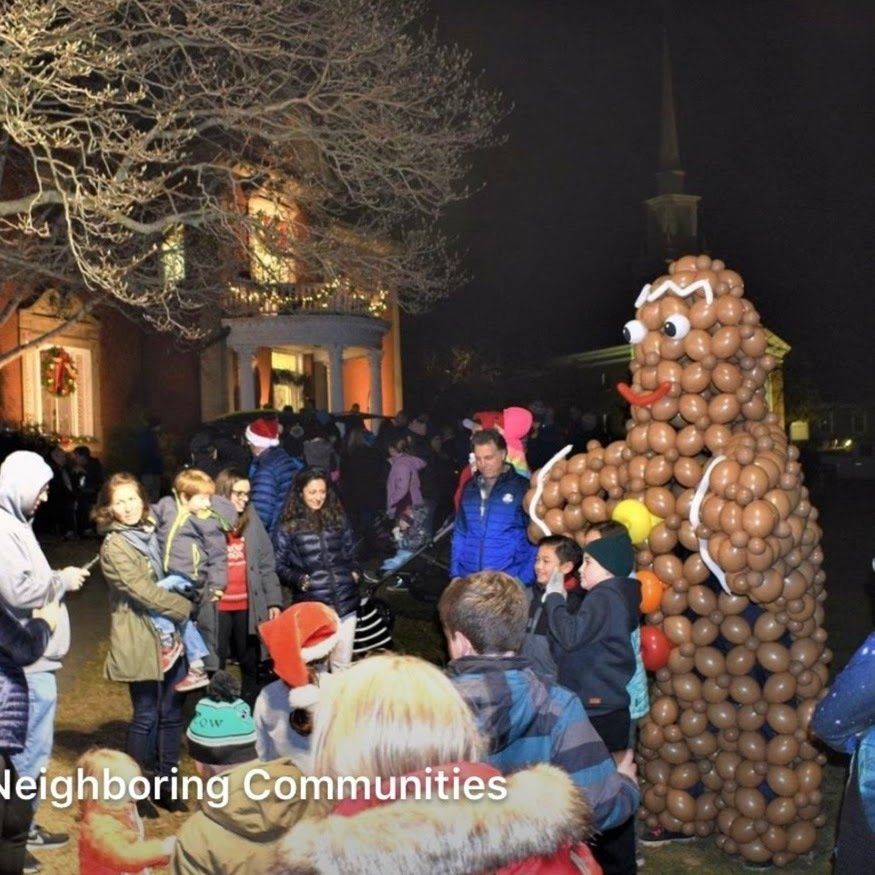 People gather at night with a large gingerbread man made of balloons, in front of a house decorated for the holidays.