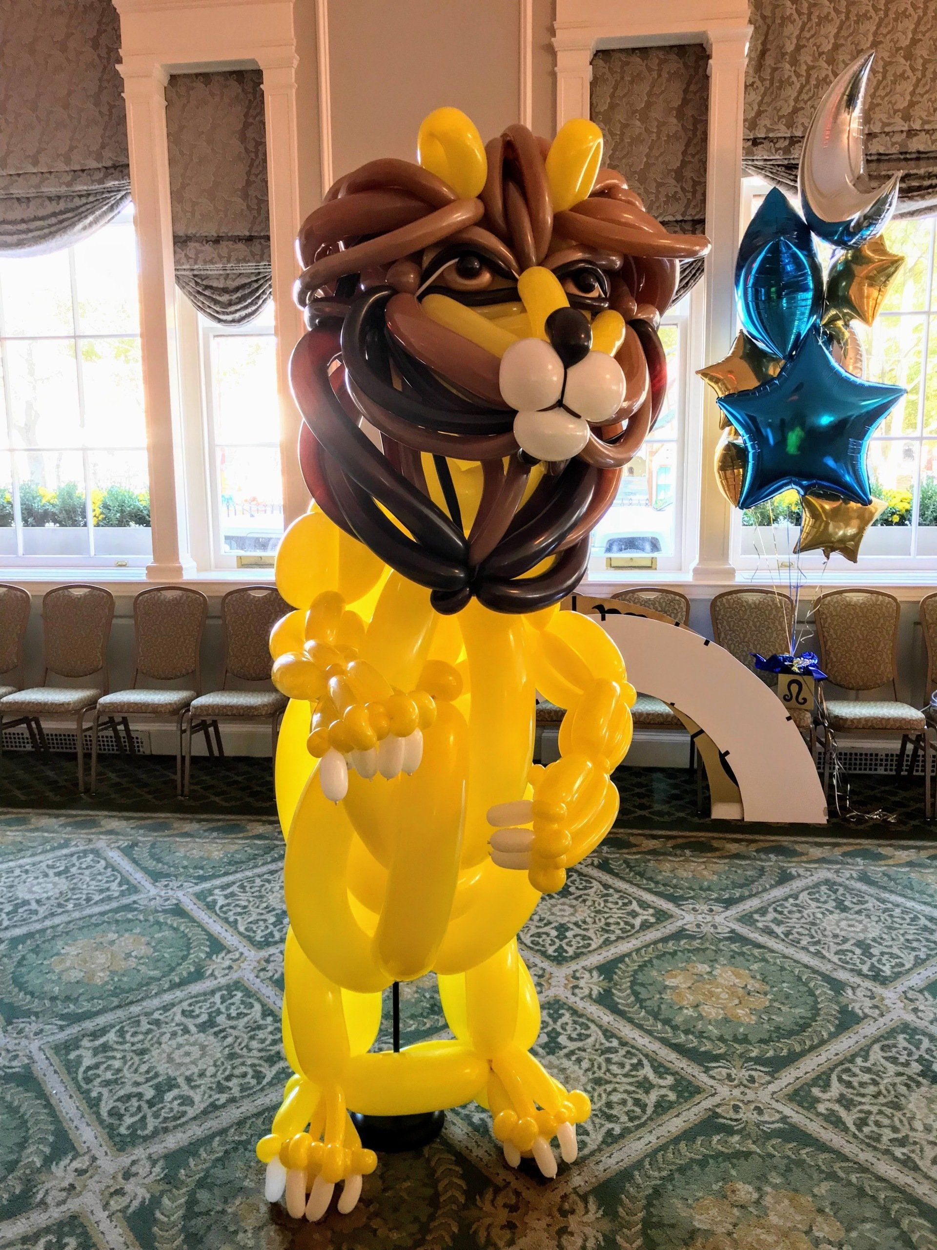 A large balloon sculpture of a yellow lion with a brown mane, standing indoors.