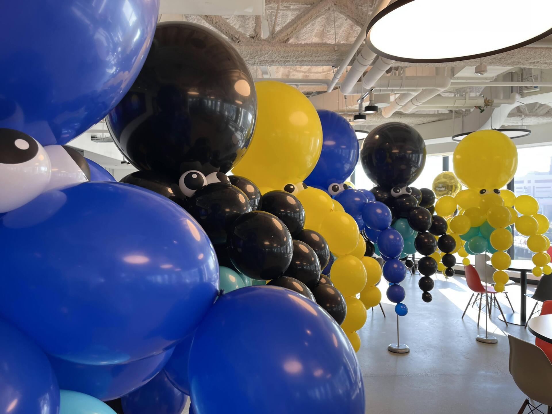 Colorful balloon animal display in an office setting. Includes blue, yellow, and black octopus and whale-like creatures.