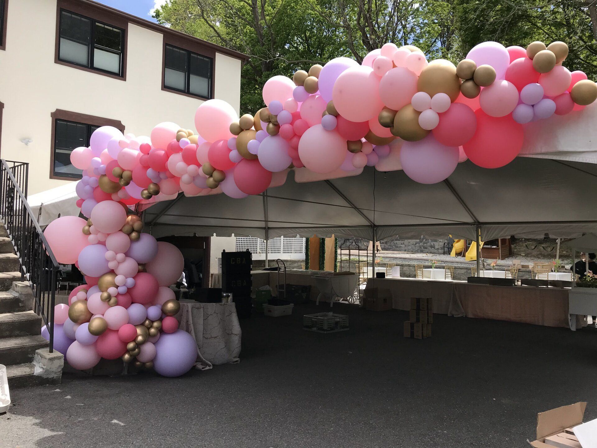 Organic balloon arch in pink, gold, and lavender around large tent outdoors.