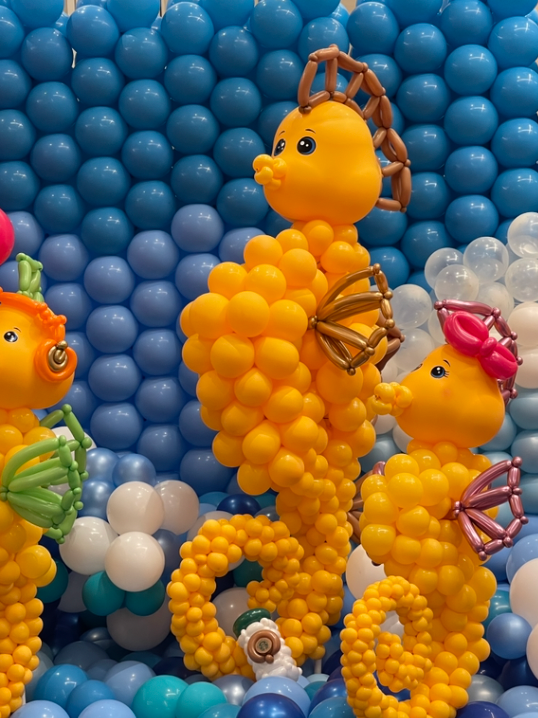 Yellow seahorse balloon sculptures against a blue and white balloon wall.