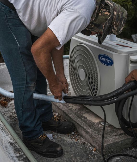 A man is working on a carrier air conditioner on a roof.