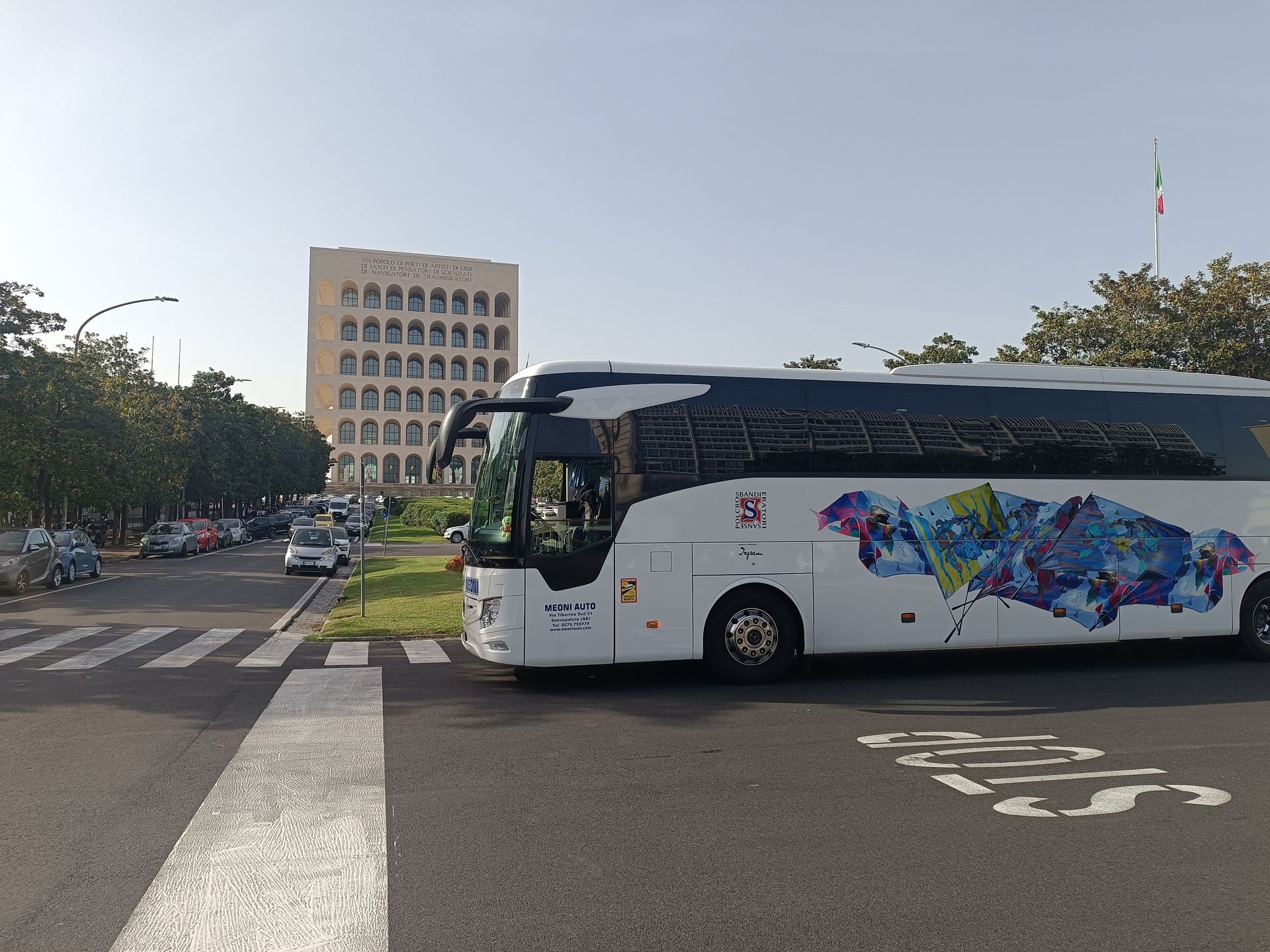 Un autobus turistico bianco attraversa una strada vicino a un edificio alto in una giornata di sole.