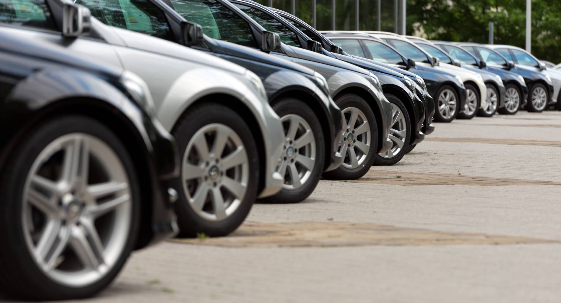 Una fila di auto parcheggiate lungo un marciapiede, viste di lato da una strada o da un parcheggio.