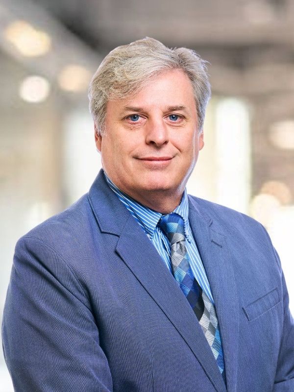 A man in a suit and tie is standing with his arms crossed.