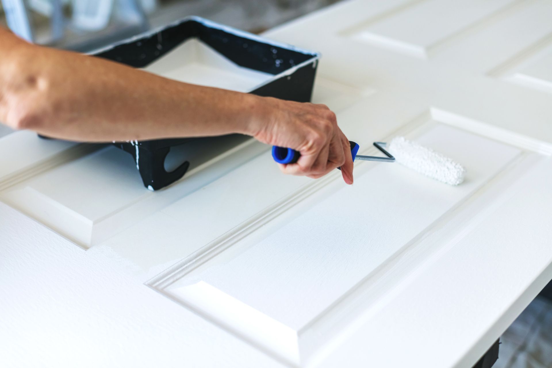 A person is painting a white door with a paint roller.