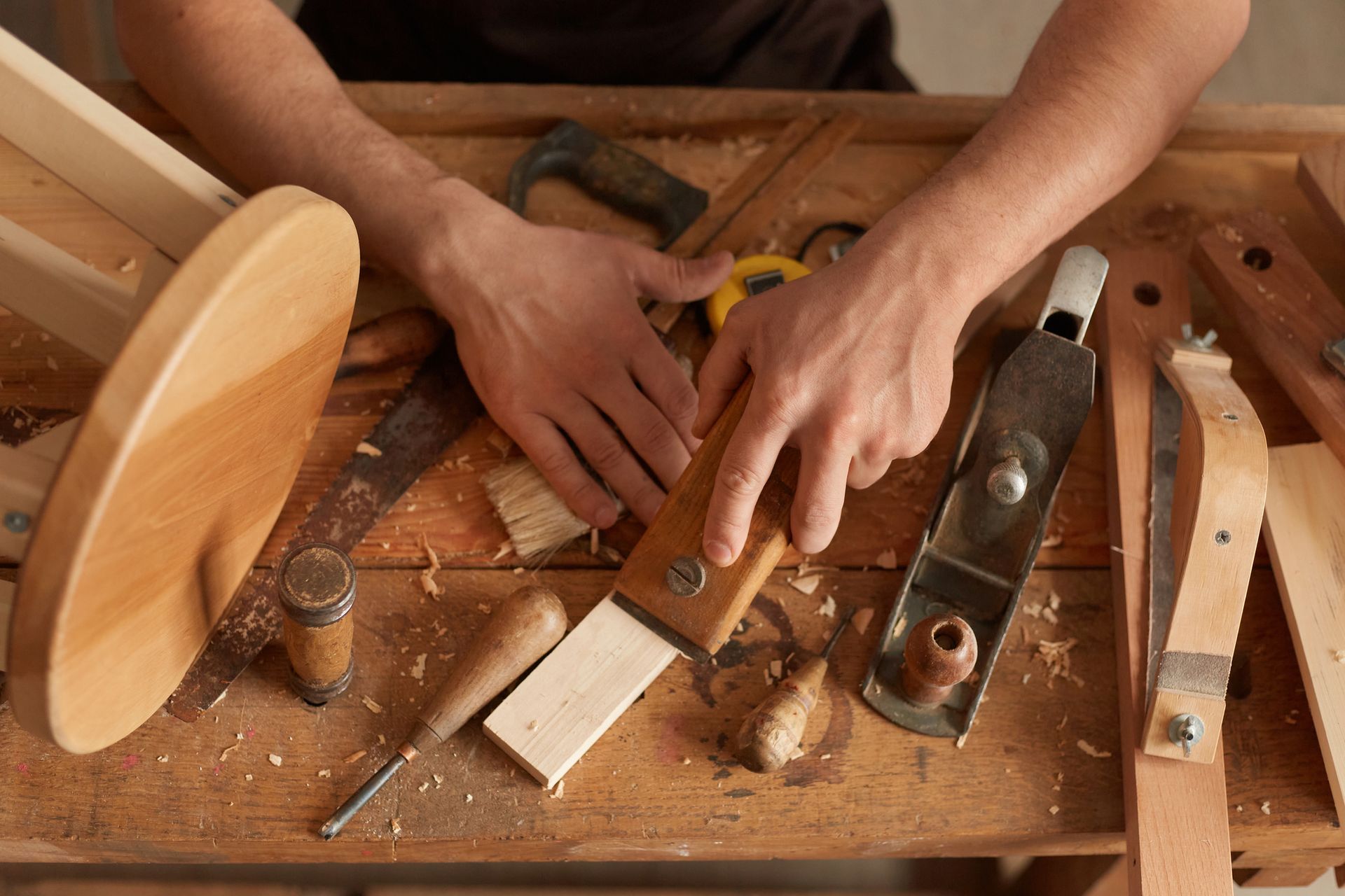A man is working on a piece of wood on a wooden workbench.