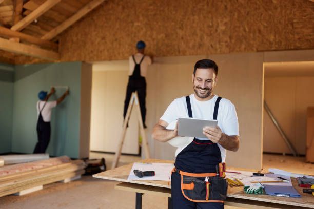 A man is holding a tablet in a room under construction.