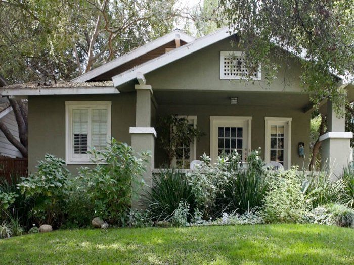 Small gray house with white trim and a lush front garden under trees