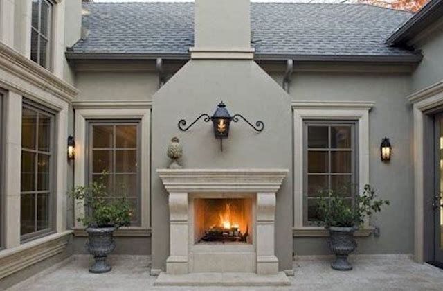 Courtyard patio with a lit outdoor fireplace, gray walls, French doors, and potted plants