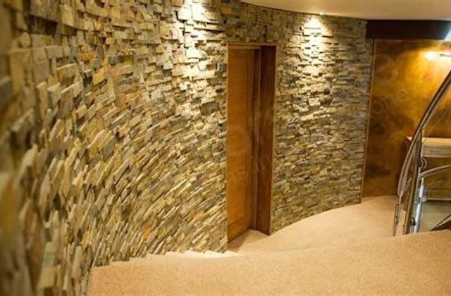 Curved hallway with stone walls, beige carpet, wooden door, and metal railing on the right