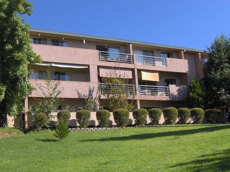 Apartment building with pink balconies, shrubs, and a green lawn under a clear blue sky