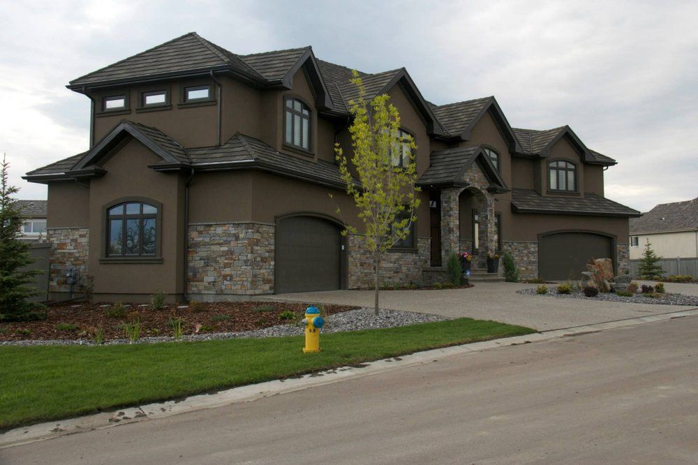 Large brown suburban house with a stone facade, green lawn, and driveway on a quiet street