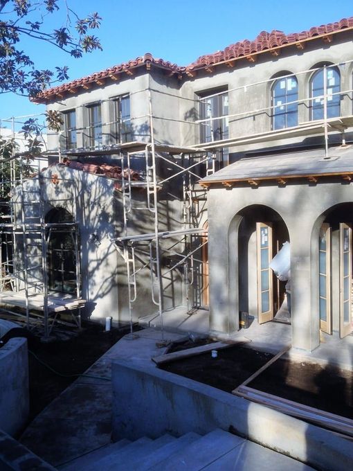 Scaffolding around a stucco house with arched windows and red tile roof under construction