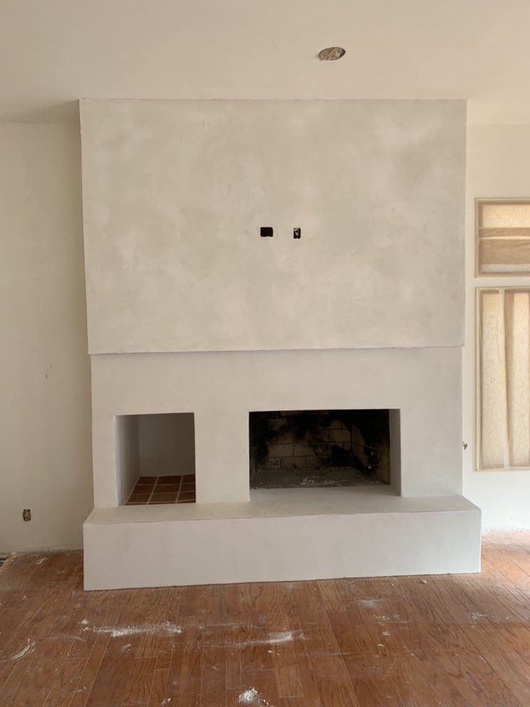 Unfinished white fireplace surround with a large opening and rough wooden floor in a room under construction