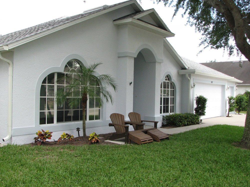 White house exterior with arched windows, front porch, lounge chairs, and green lawn