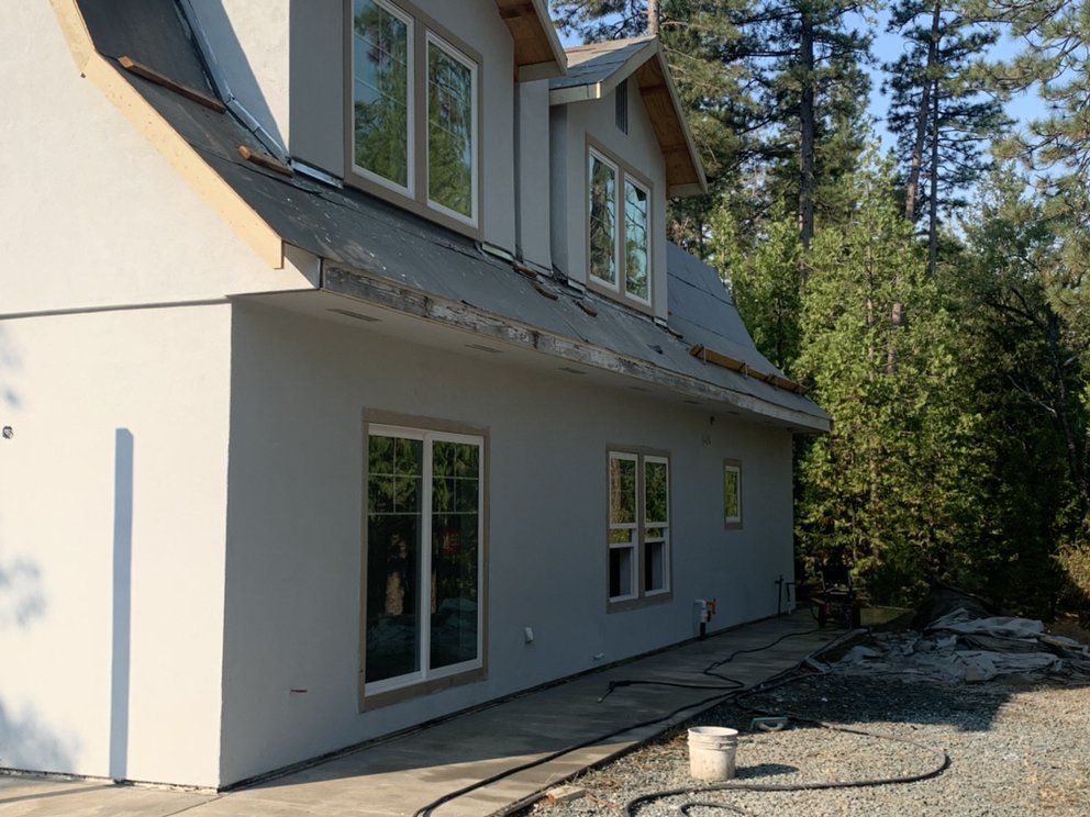 Gray two-story house exterior with large windows beside a wooded area