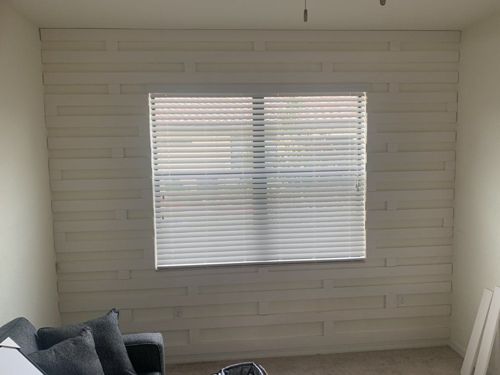 Empty white room with a window and closed blinds, gray sofa corner in the foreground