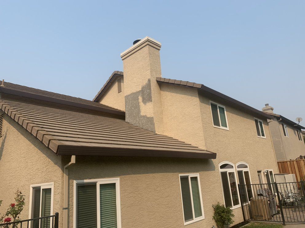 Suburban house with beige stucco walls, brown roof, and green-trimmed windows under a clear blue sky