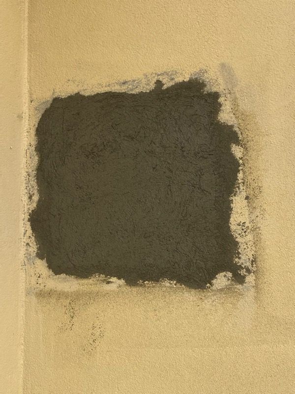 Dark gray square patch on a beige wall.
