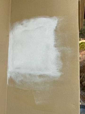 White paint patch on a cardboard surface, with a blurred outdoor background.