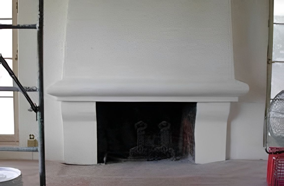 White fireplace mantel with dark firebox in a bright room, with a small window and ladder at left.