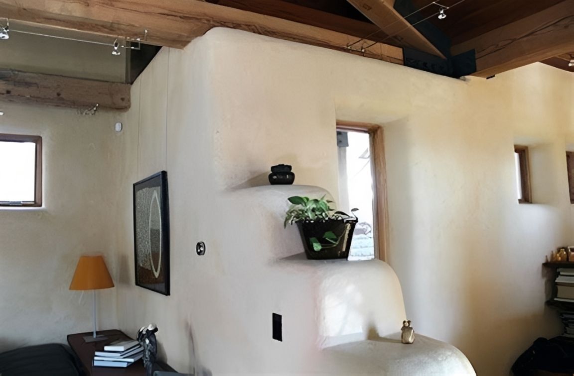 Bright, white interior room with wood beams, small windows, and a table lamp beside a potted plant.