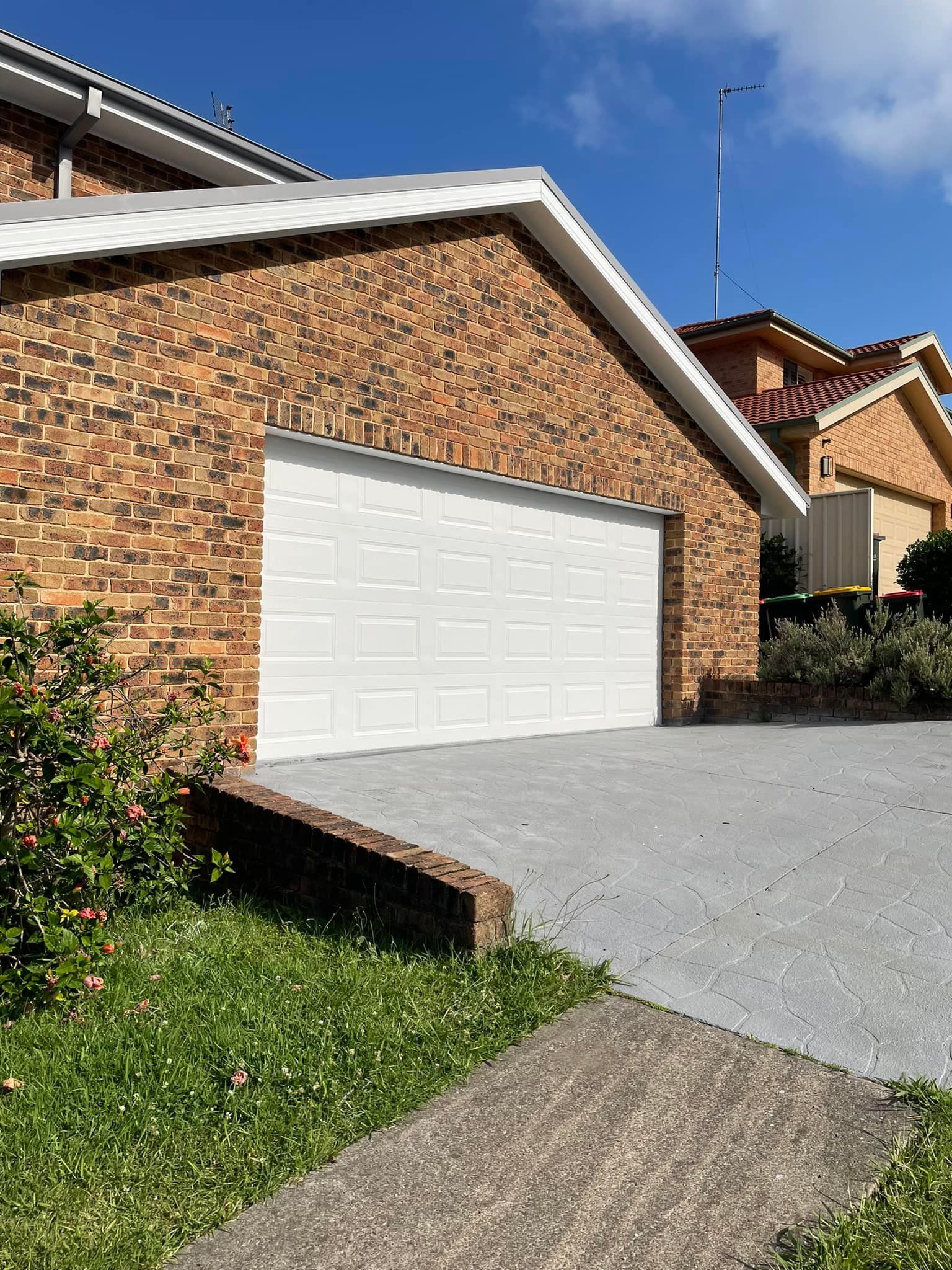 A Brick House With a White Garage Door and a Driveway — Karl Witt Painter & Decorator In Albion Park, NSW