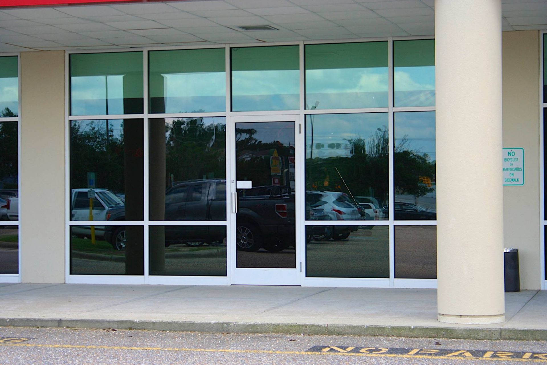 Exterior view of a commercial building entrance with glass windows, a single glass door, and a white support column.