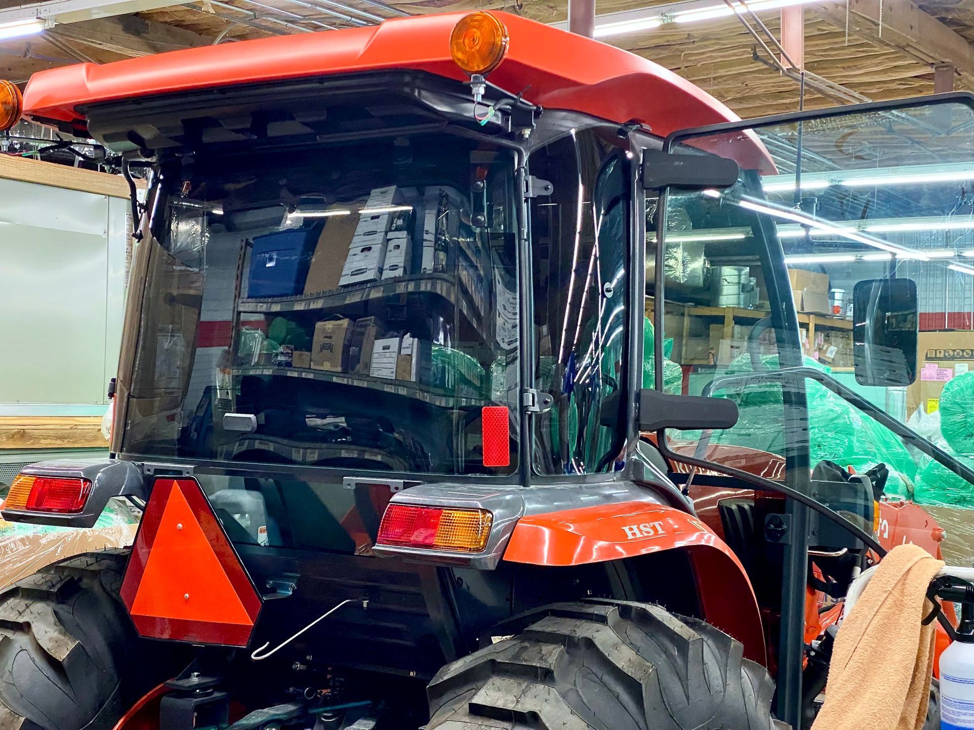 Rear view of an orange tractor parked indoors, showing the cab, large tires, and a triangular red slow-moving vehicle sign.