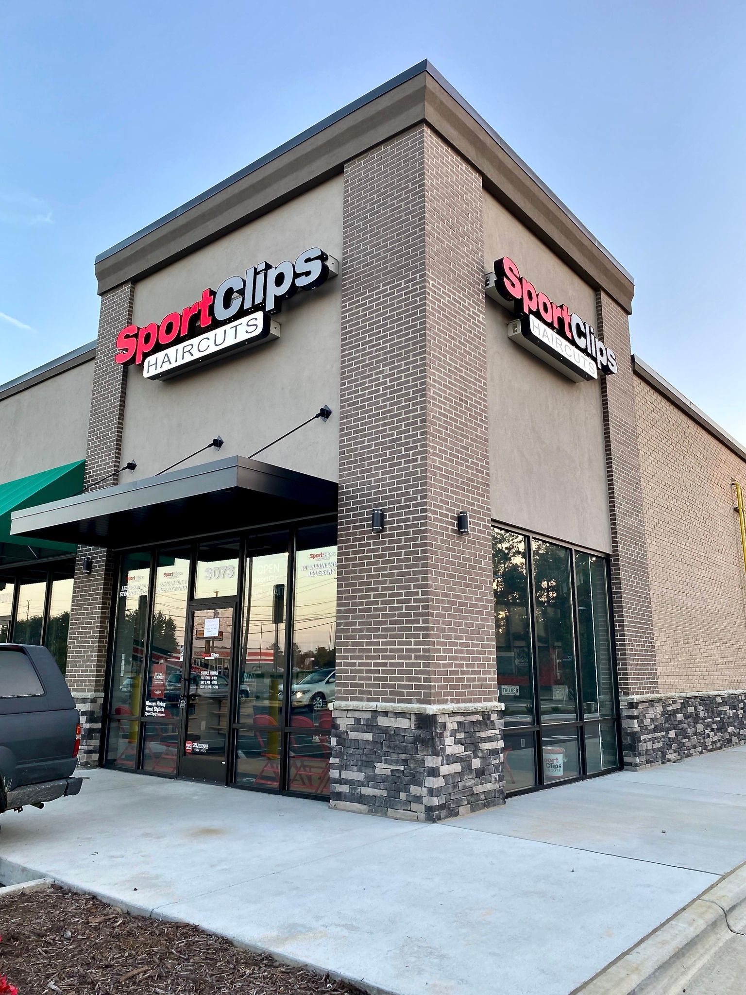 Exterior view of a Sport Clips Haircuts storefront with tan walls, stone accents, and glass windows under a clear sky.