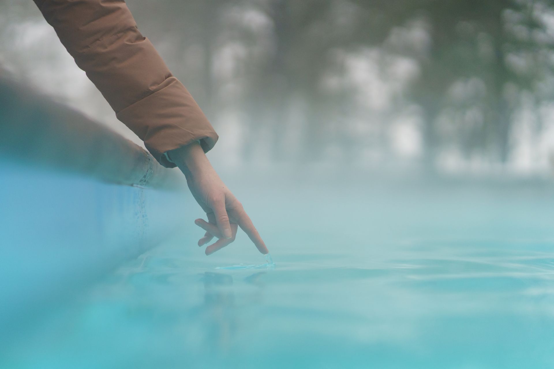 Hand testing outdoor pool water temperature in winter season