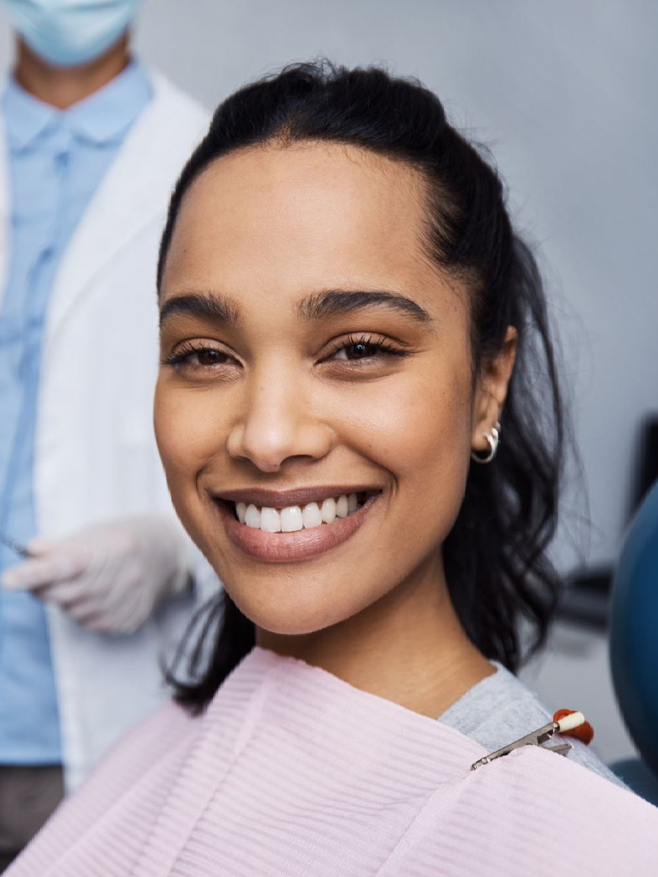 A woman is smiling while sitting in a dental chair.