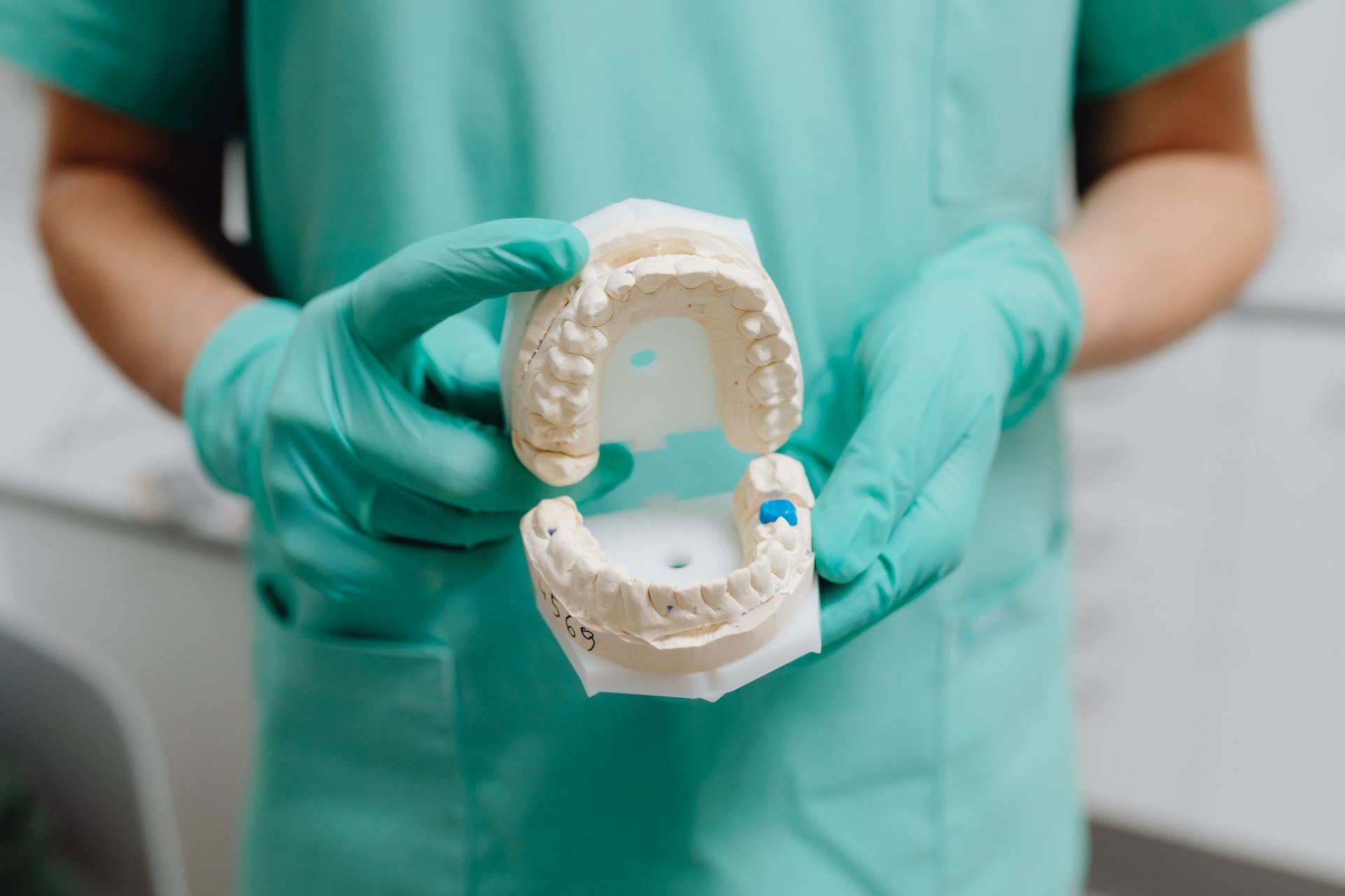 Dentist holding a dental mold showing gums and teeth, with green scrubs in the background