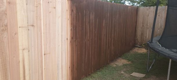Weathered wooden fence along a narrow backyard path beside a trampoline