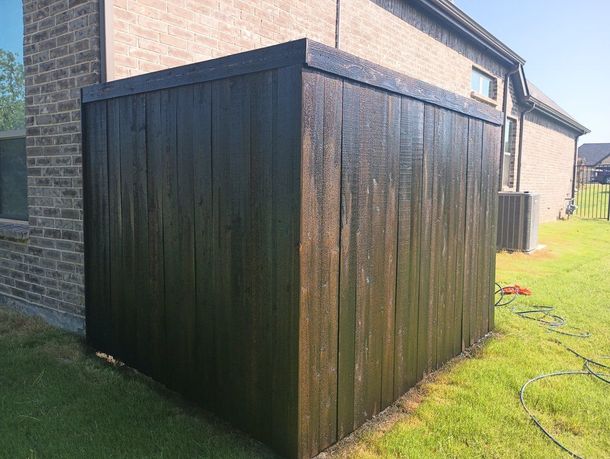 Dark wooden shed attached to a brick house beside a grassy yard, with hoses on the ground.