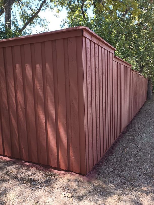 Long red wooden fence extending along a dirt path under trees