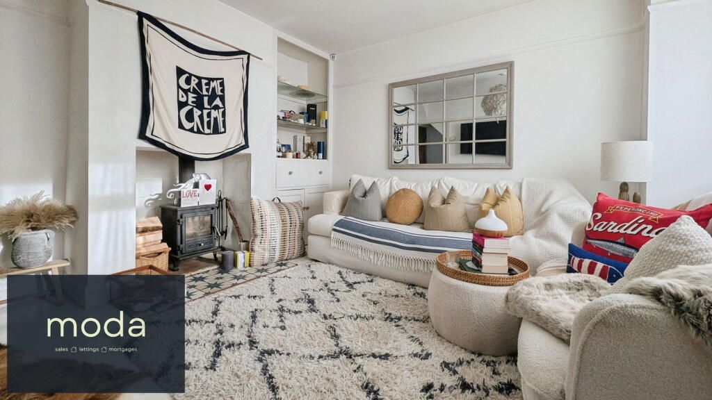 Cozy living room with white walls, patterned rug, sofa with pillows, and a wood-burning stove.