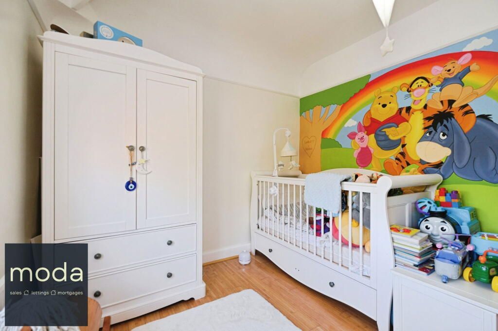 A bright white nursery with a crib and wardrobe featuring a Winnie the Pooh mural.