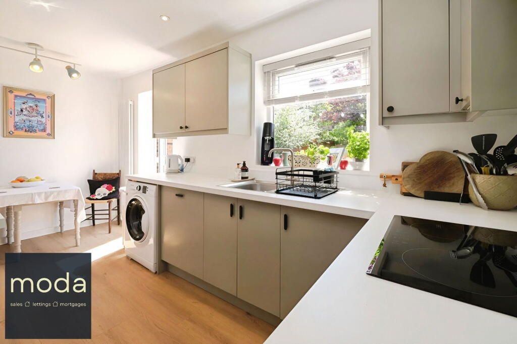 Kitchen with light wood floor, beige cabinets, a window, and a washing machine.