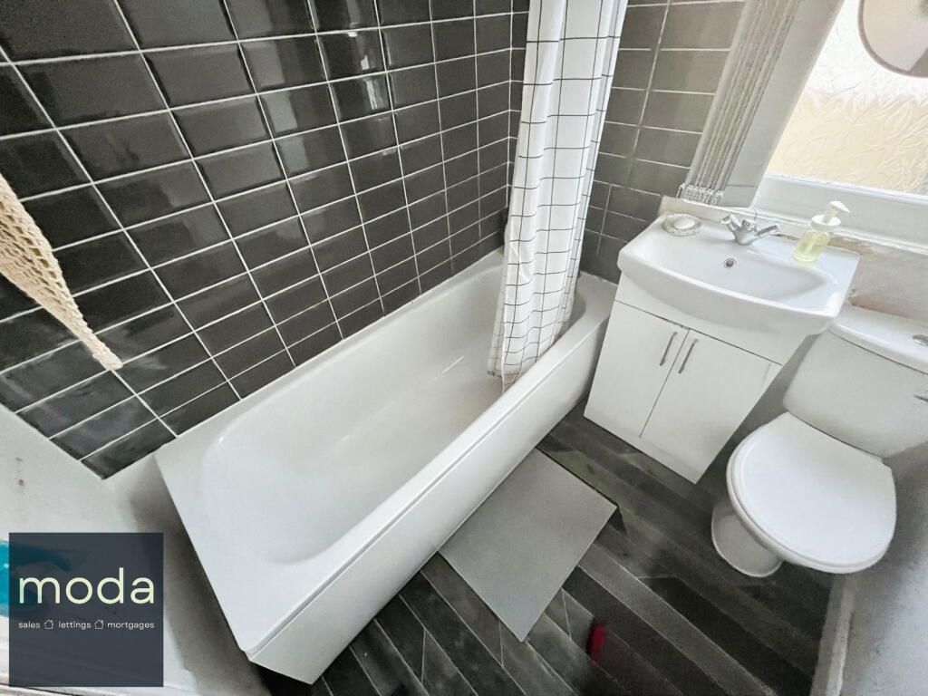 Bathroom with black tiled wall, white tub, sink, and toilet; dark grey floor.