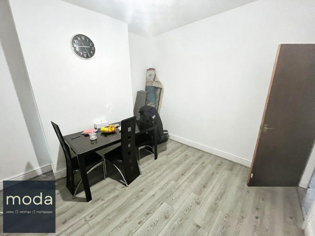 Dining area with black table, chairs, clock on wall, door. Gray wood-look flooring.