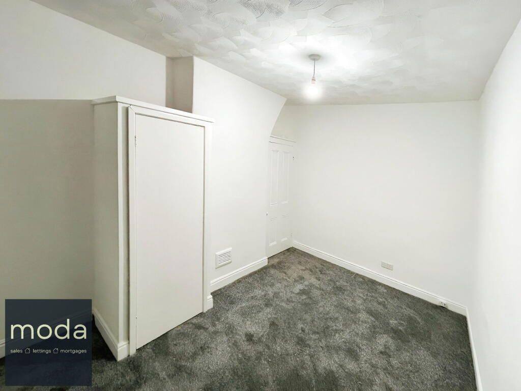 Empty, white bedroom with gray carpet and a wardrobe; overhead light.